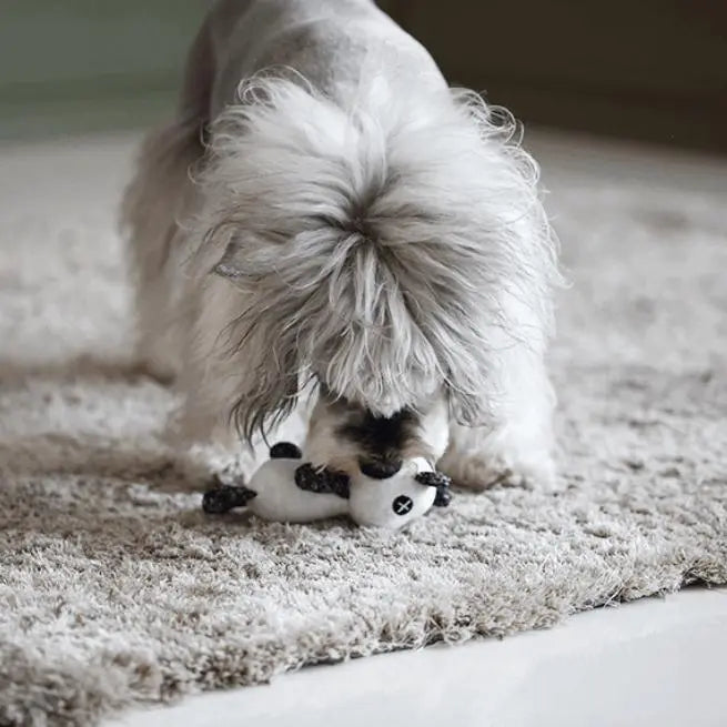 A plush toy designed for dogs, featuring a black and white panda shape with distinctive X-shaped eyes. Made from soft, knitted fabric, the toy is lightweight and cuddly, suitable for small to medium-sized dogs. It has a squeaker embedded inside for interactive play and is crafted with pet-safe materials for durability and comfort. The toy's design is both visually appealing and functional, promoting dental health and reducing anxiety through engaging play.